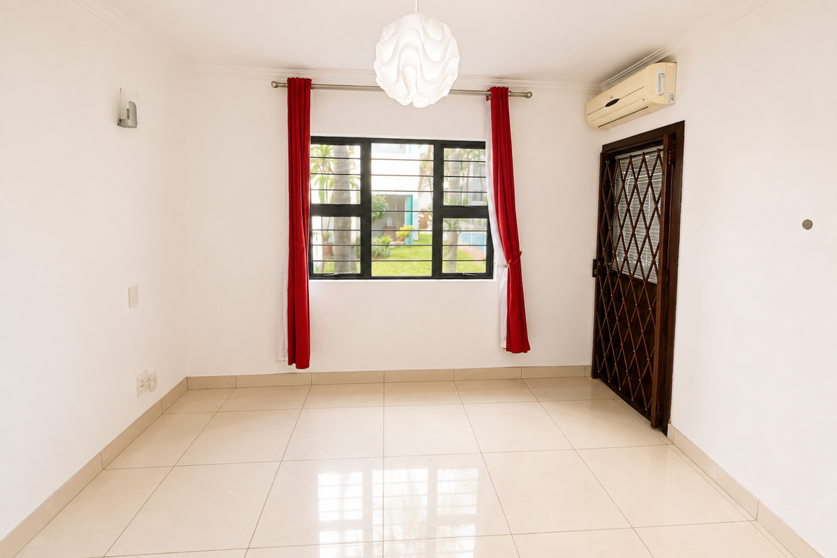 A bright, empty living area featuring neutral tiled flooring, an installed air conditioning unit, and a security gate leading to the exterior.
