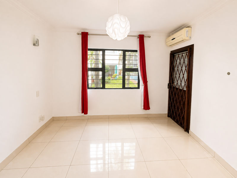 A bright, empty living area featuring neutral tiled flooring, an installed air conditioning unit, and a security gate leading to the exterior.