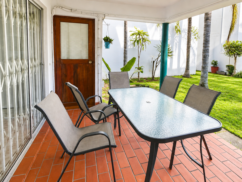 A covered patio area featuring terracotta-style tiling, a security gate, and direct access to a shared garden space.