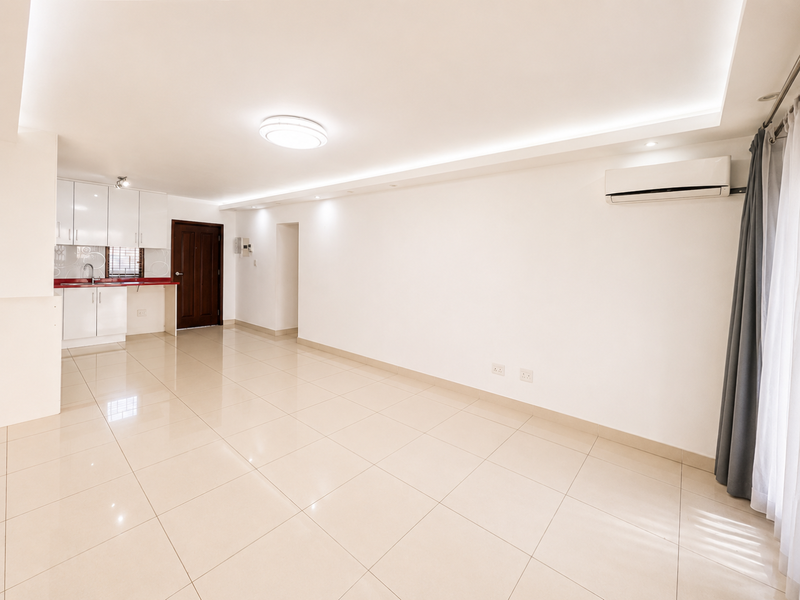 Spacious open-plan living area featuring tiled floors, recessed lighting, a wall-mounted air conditioner, and a compact kitchen with white cabinetry and a red countertop.