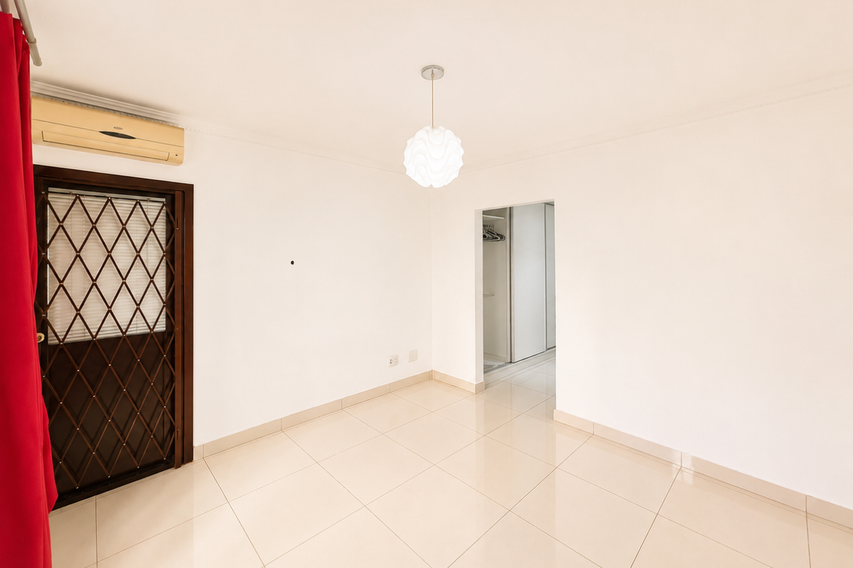 A bright, empty bedroom featuring tiled flooring, a built-in wardrobe, a security gate, and a wall-mounted air conditioning unit.