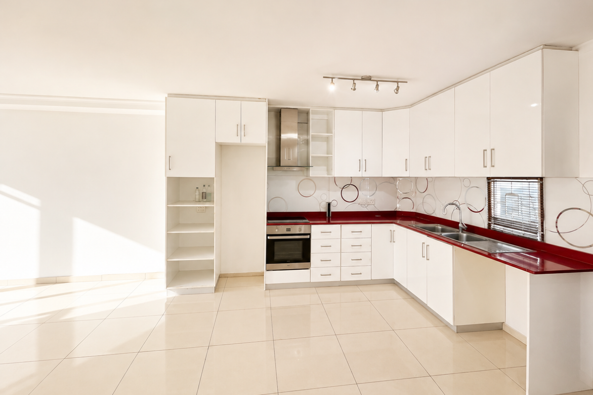 A clean, modern kitchen featuring white cabinetry, a striking red countertop, stainless steel appliances, and neutral tiled flooring in an open-plan layout.