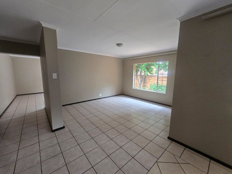 A spacious, empty living area featuring neutral wall paint, ceramic tiled flooring, and a large window providing natural light.