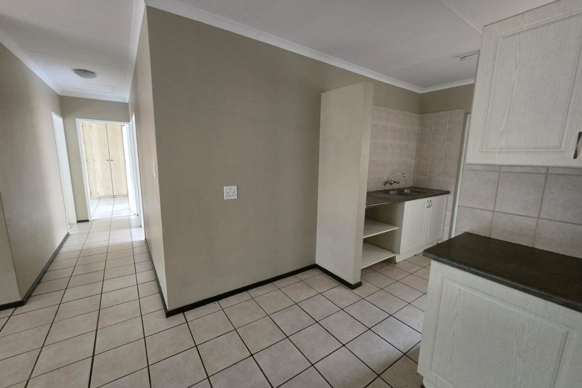 A functional kitchen area featuring built-in cabinetry, laminate countertops, and tiled flooring, leading into a hallway with built-in storage.