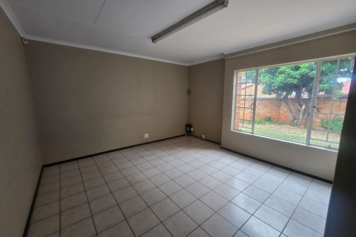 An empty living room featuring neutral tiled flooring, a large window overlooking the garden, and a simple ceiling-mounted light fixture.
