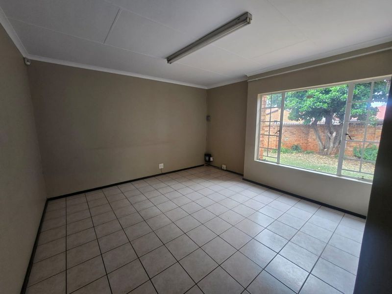 An empty living room featuring neutral tiled flooring, a large window overlooking the garden, and a simple ceiling-mounted light fixture.