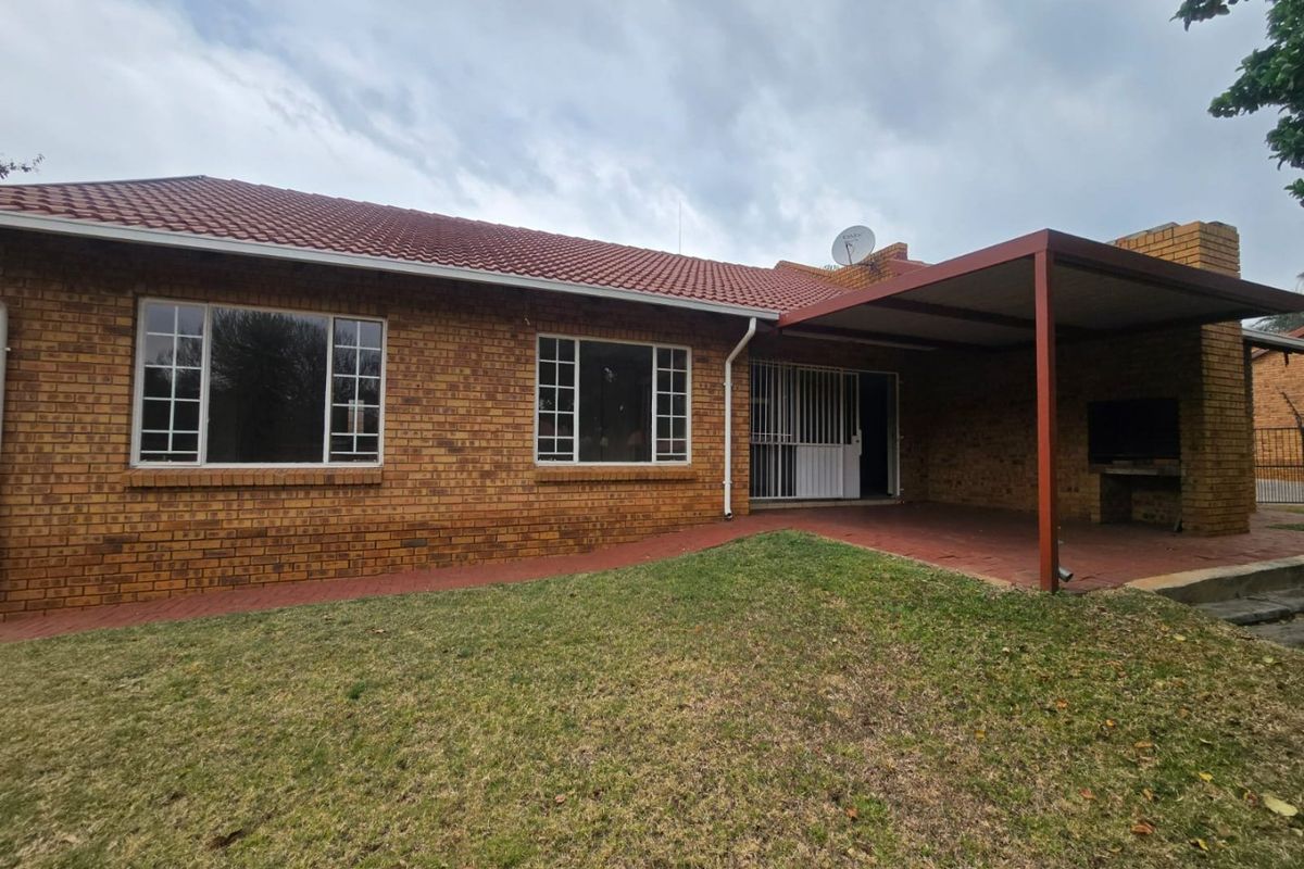 Rear view of a face brick house featuring a covered patio with a built-in braai, tiled roof, and a small garden area.