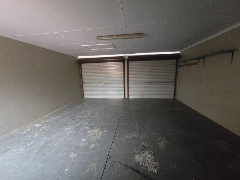 A spacious double garage featuring dual roller doors, concrete flooring, and wall-mounted storage brackets, providing ample secure parking and utility space.