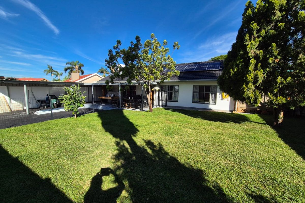 Rear view of the property featuring a well-maintained lawn, a covered patio area, and roof-mounted solar panels.
