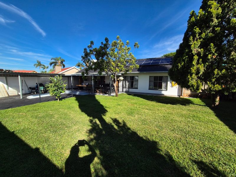 Rear view of the property featuring a well-maintained lawn, a covered patio area, and roof-mounted solar panels.