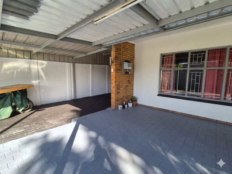 A covered outdoor patio area featuring paved flooring, a brick support pillar, and a corrugated metal roof structure.
