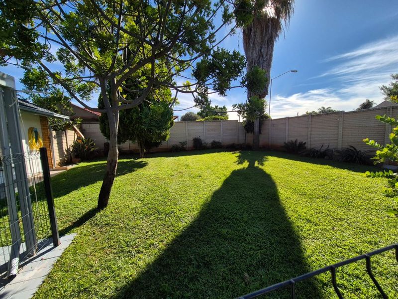 A well-maintained private backyard featuring a lush green lawn, mature trees, and secure brick boundary walls.
