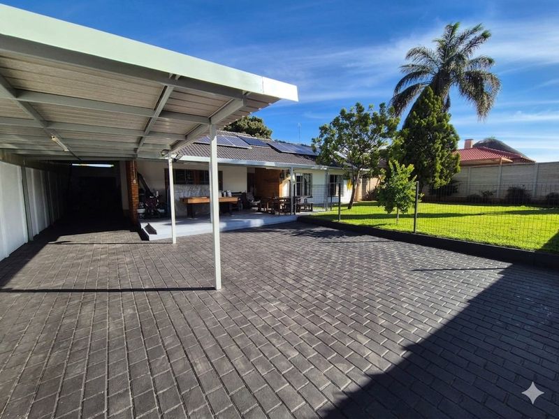 Rear exterior view featuring a paved driveway, covered carport, solar panels on the roof, and a well-maintained garden with lawn and fencing.