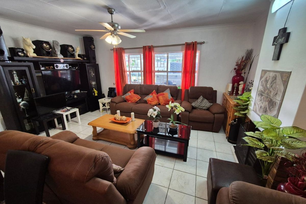 A comfortable living room featuring tiled flooring, a ceiling fan, and large windows with security bars, providing a functional and well-lit space.