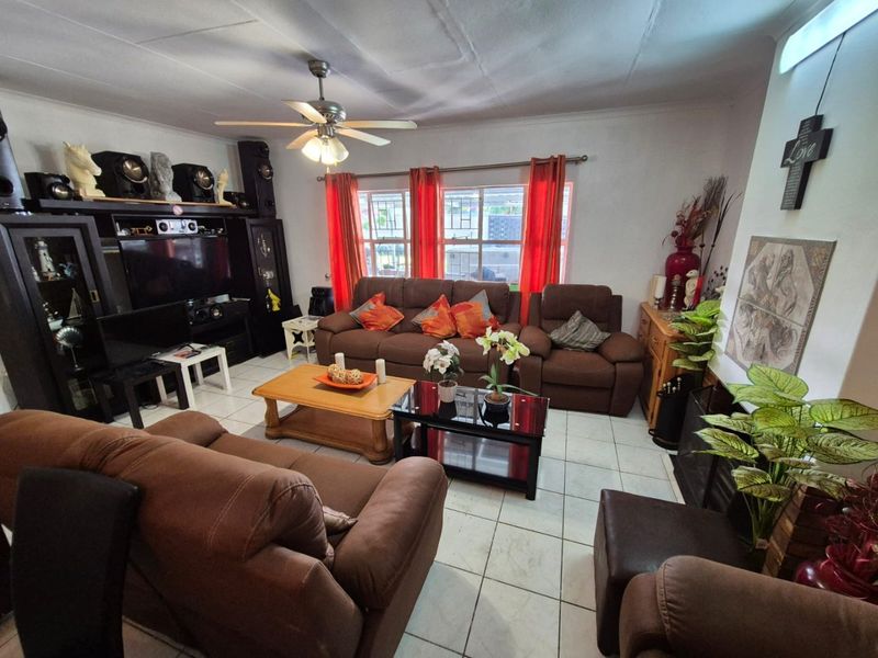 A comfortable living room featuring tiled flooring, a ceiling fan, and large windows with security bars, providing a functional and well-lit space.