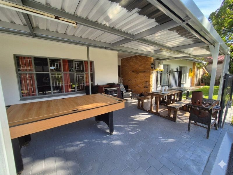 A covered outdoor patio area featuring paved flooring, exposed brickwork, and a corrugated metal roof structure, suitable for outdoor entertaining.