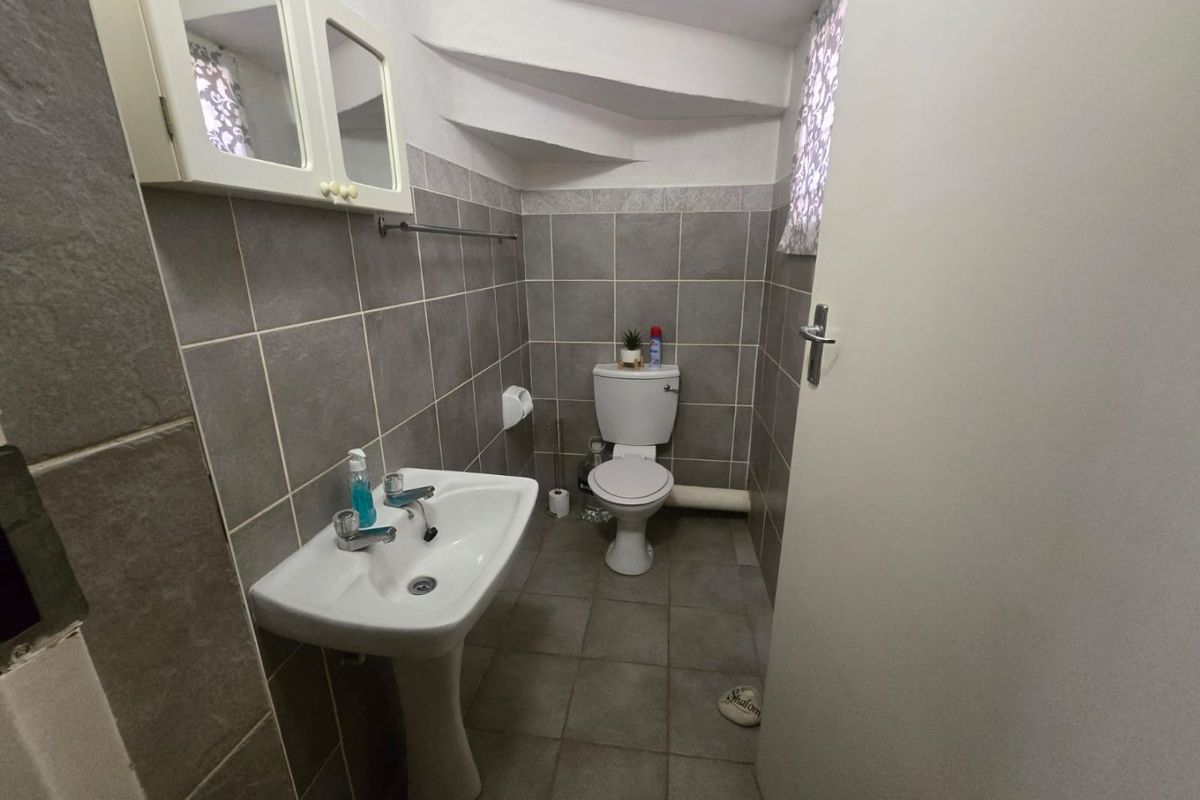 A compact bathroom featuring tiled walls and flooring, a pedestal sink, and a toilet, situated under a staircase.