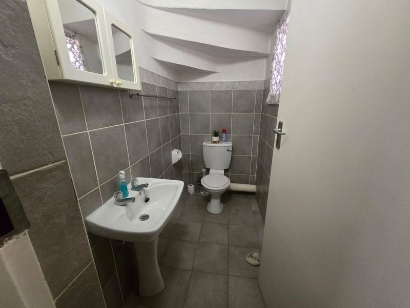 A compact bathroom featuring tiled walls and flooring, a pedestal sink, and a toilet, situated under a staircase.