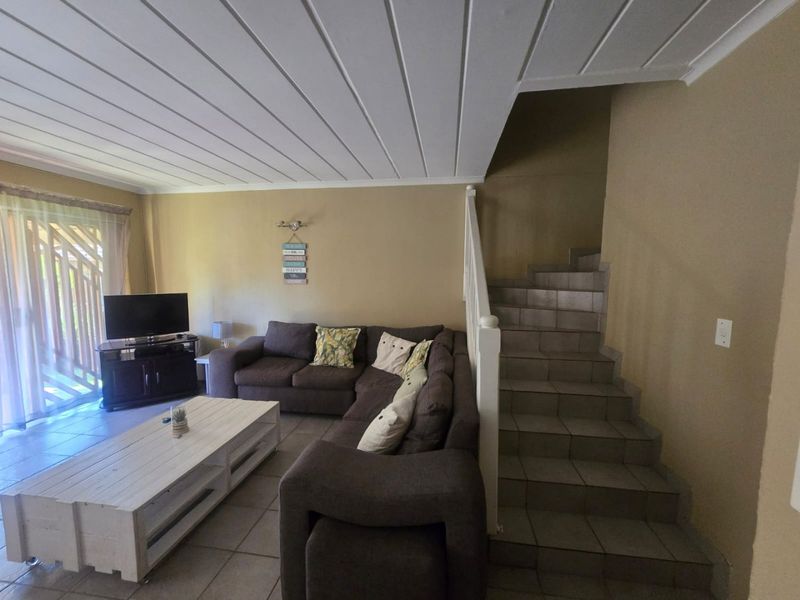A living room featuring tiled flooring, a staircase with a white balustrade, and a timber panelled ceiling, with access to an outdoor area.