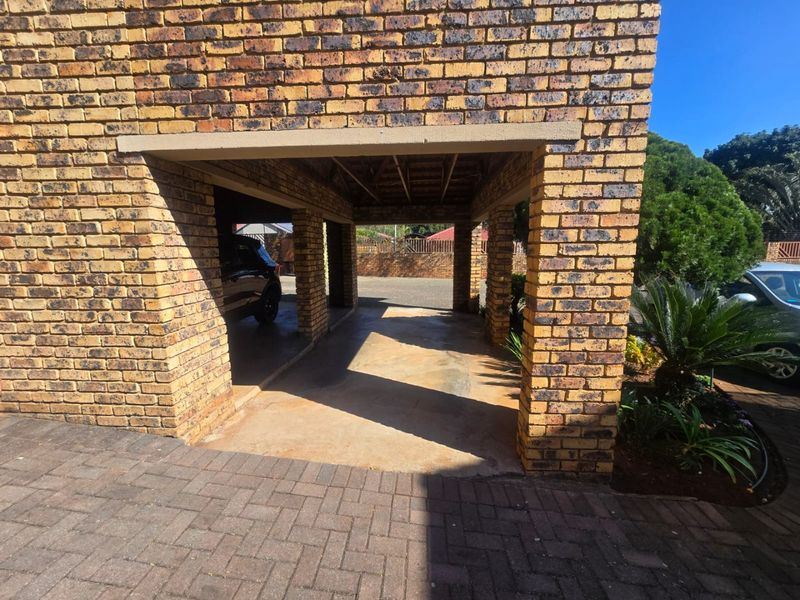 A covered carport area featuring face brick pillars and exposed timber roof structure, providing sheltered parking space.