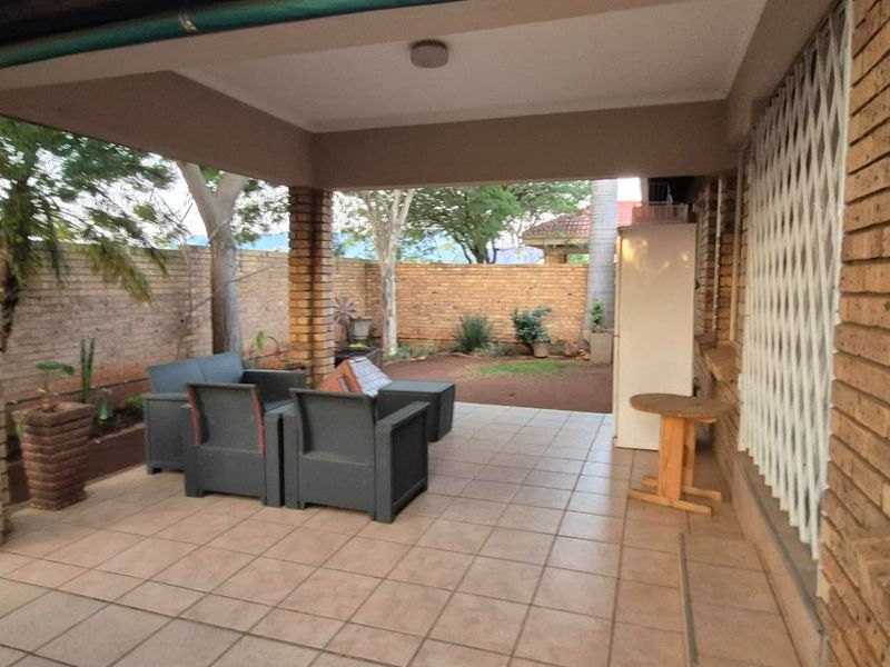 A covered patio area featuring tiled flooring and brick pillars, overlooking a private garden space with brick boundary walls.
