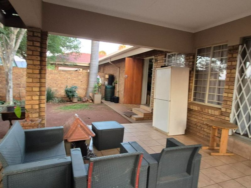 A covered patio area featuring tiled flooring and brick pillars, providing access to the rear garden through a sliding door with security gate.