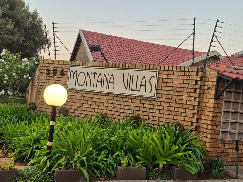 Entrance signage and brick boundary wall for Montana Villas townhouse complex, featuring electric fencing and established garden landscaping.