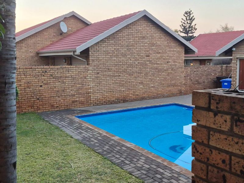 A private outdoor pool area featuring a paved surround, brick boundary walls, and a view of the townhouse exterior with a tiled roof.