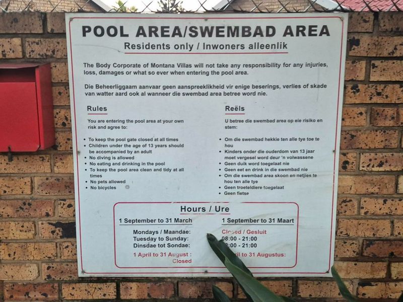 A signage board displaying pool area rules and operating hours mounted on a brick boundary wall.
