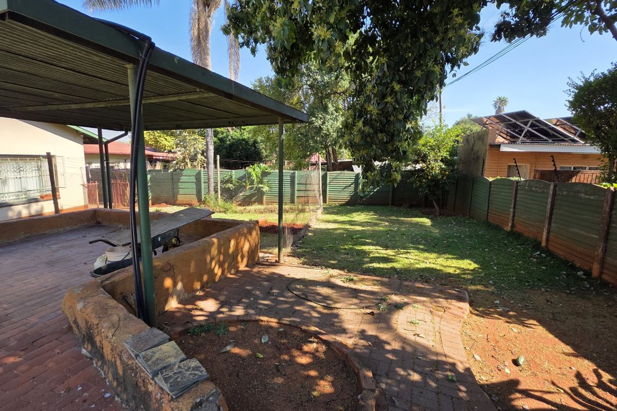 Rear garden area featuring a covered patio with brick paving, a retaining wall, and perimeter precast concrete fencing.
