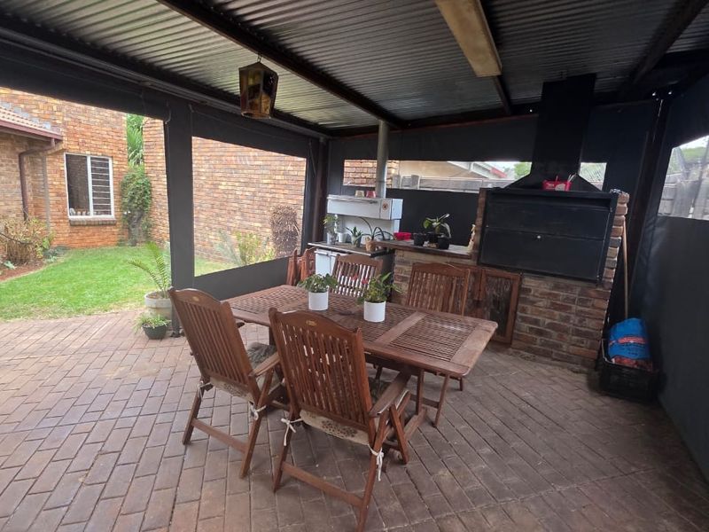 Covered outdoor patio featuring brick paving, a built-in brick braai, and retractable canvas blinds, overlooking the rear garden area.