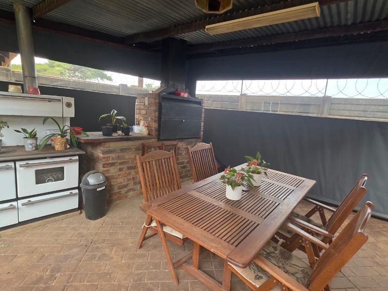 Covered outdoor patio area featuring a built-in brick braai, paved flooring, and protective roll-down canvas blinds for all-weather use.