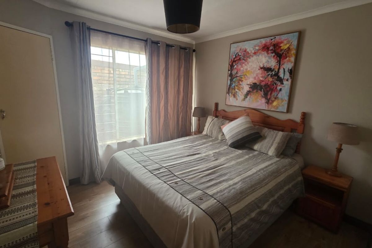 A cozy bedroom featuring laminate flooring, a built-in cupboard, and security bars on the window.