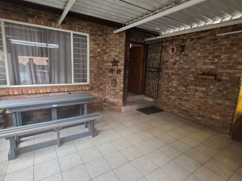 A covered patio area featuring exposed brick walls, tiled flooring, and a corrugated metal roof, providing a functional outdoor space.