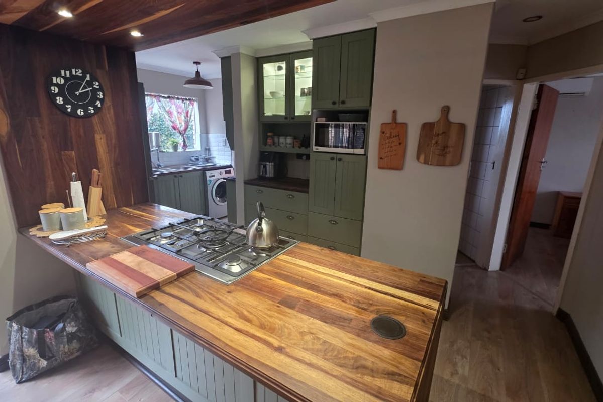A well-appointed kitchen featuring a wooden breakfast bar with an integrated gas hob, olive green cabinetry, and built-in appliances.