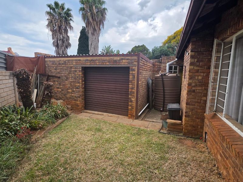 Rear exterior view showing a face brick garage, water storage tank, and a small garden area with security bars on the windows.