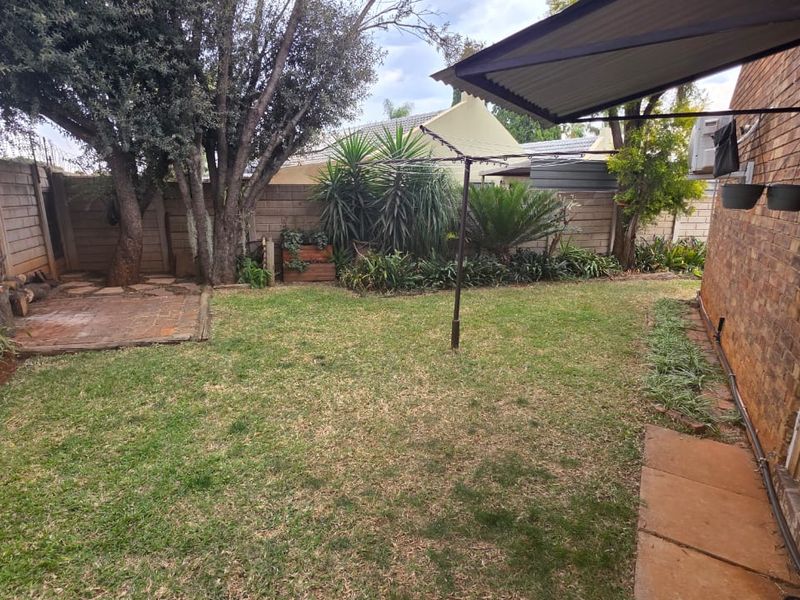 A private rear garden featuring a lawn, brick paved section, boundary walls, and a fixed rotary clothesline.