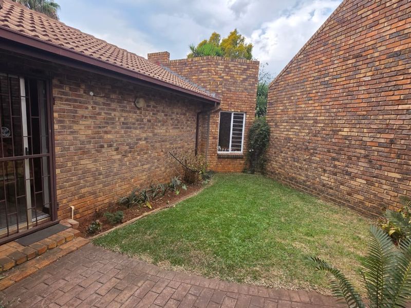A private rear courtyard featuring a brick-walled exterior, a small lawn area, and a paved patio space accessible via a sliding door.