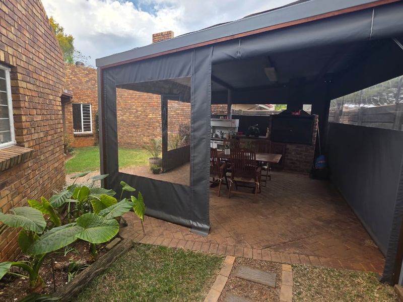 Covered outdoor patio area featuring brick paving, a built-in braai, and protective canvas drop-down blinds, ideal for year-round outdoor entertaining.