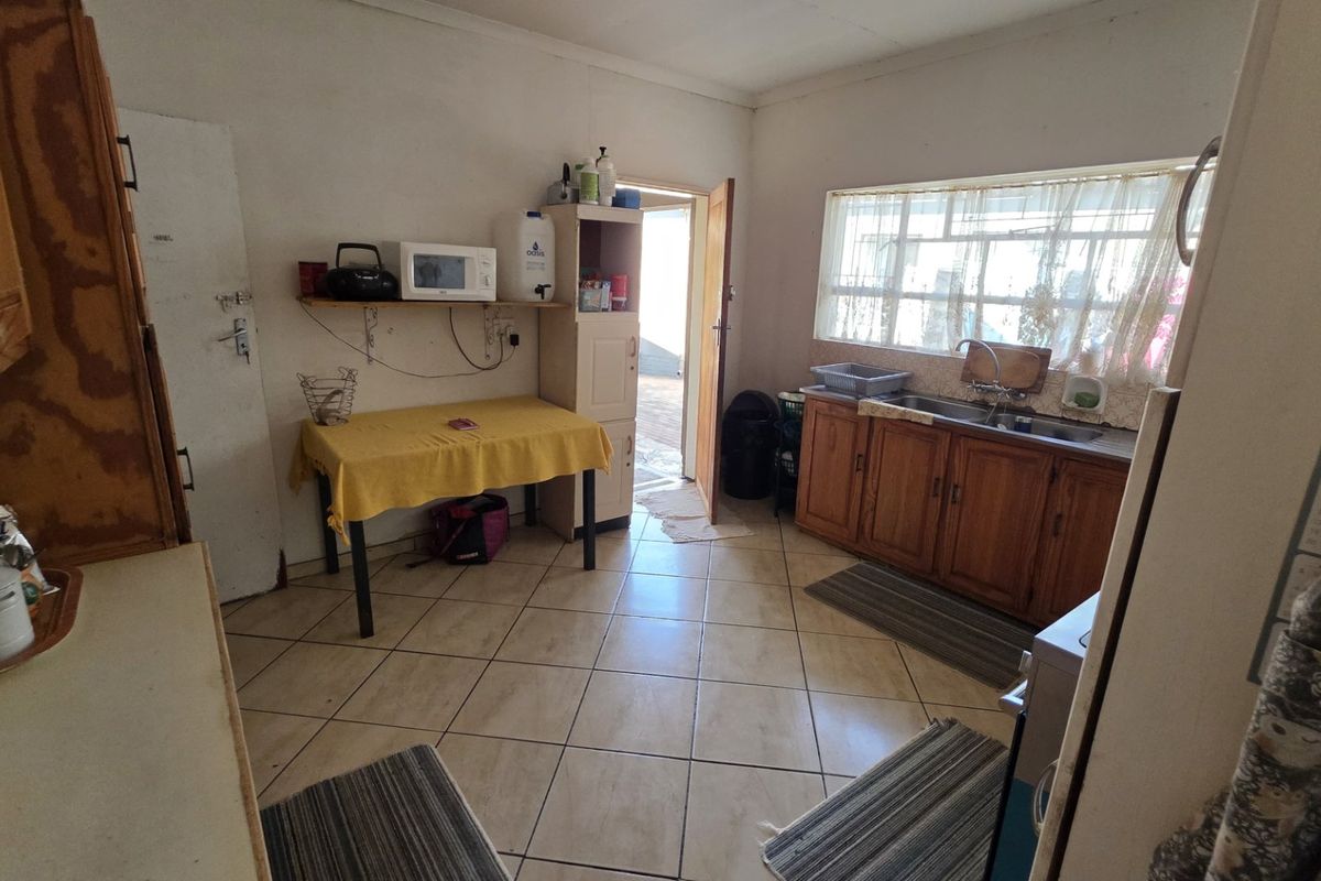 A functional kitchen featuring tiled flooring, wooden cabinetry, and a stainless steel sink, offering potential for modernization and cosmetic updates.