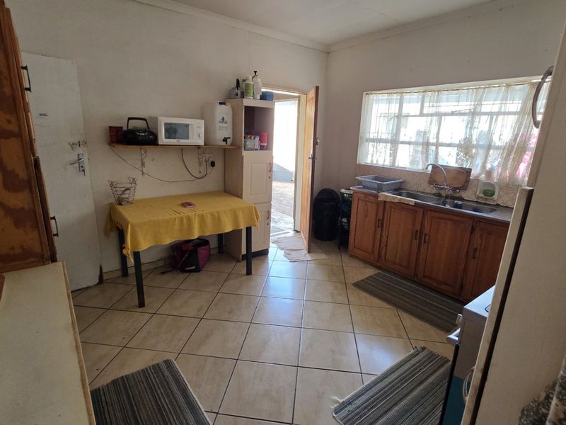 A functional kitchen featuring tiled flooring, wooden cabinetry, and a stainless steel sink, offering potential for modernization and cosmetic updates.
