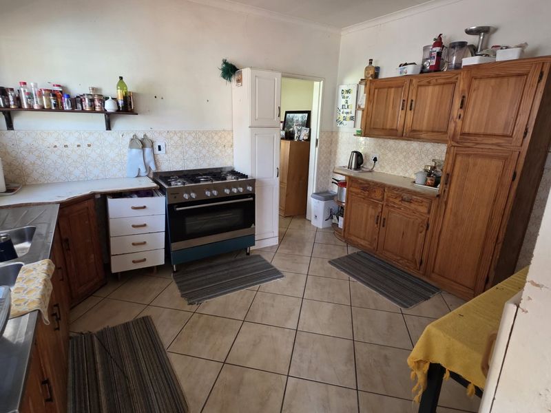 A functional kitchen featuring wooden cabinetry, a gas stove with oven, double sink, and tiled flooring, offering potential for modernization.