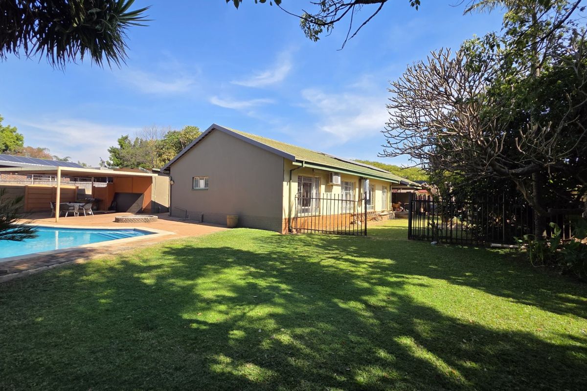Rear exterior view of the property featuring a swimming pool, paved patio area, and a well-maintained lawn with perimeter fencing.