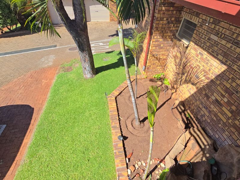 An elevated view of the front exterior featuring a brick facade, a well-maintained lawn, and a landscaped garden bed with brick edging.