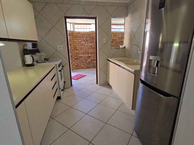 A functional kitchen featuring tiled flooring, ample built-in cabinetry, countertops, and a double sink, with direct access to an outdoor courtyard area.
