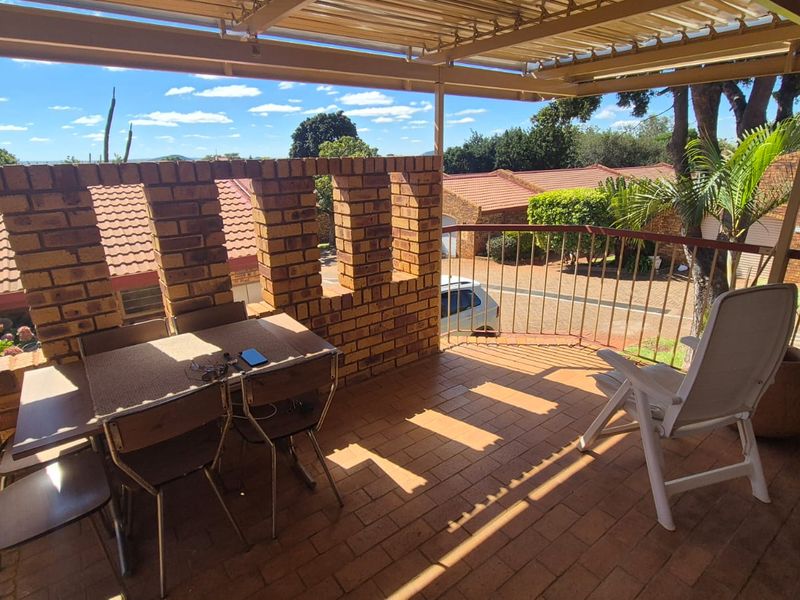 A covered balcony featuring a brick balustrade, tiled flooring, and metal roofing, offering an outdoor space with views of the surrounding townhouse complex.