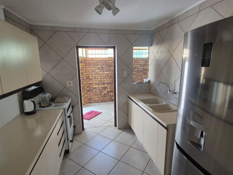 A functional kitchen featuring tiled flooring, built-in cabinetry, a double basin sink, and a freestanding stove, with direct access to an outdoor area.