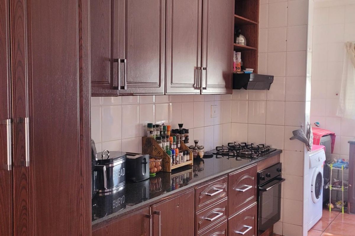 A functional kitchen featuring dark wood cabinetry, granite countertops, a gas hob, built-in oven, and tiled finishes throughout.