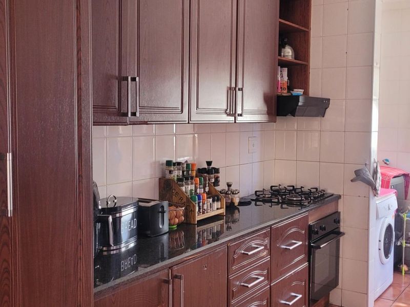 A functional kitchen featuring dark wood cabinetry, granite countertops, a gas hob, built-in oven, and tiled finishes throughout.