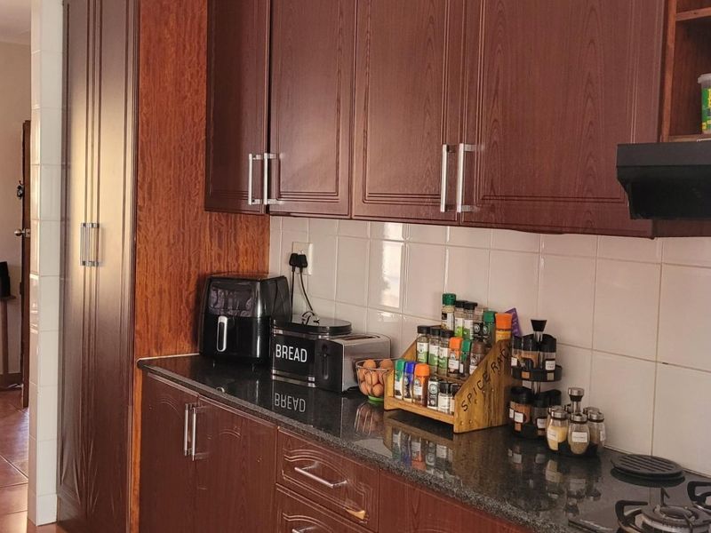 A functional kitchen featuring dark wood cabinetry, granite countertops, a gas hob, and a tiled backsplash, with an adjacent dining area.